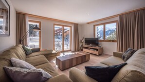 A modern living room with a sofa, a coffee table, a TV, and large windows with curtains. - Chalet Brunner 2 (Lauterbrunnen)