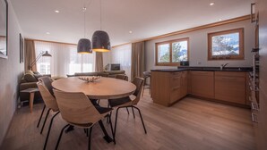 A modern kitchen with wooden cabinets, a dining area with a round table and chairs, and large windows with a view of the outdoors. - Chalet Brunner 2 (Lauterbrunnen)