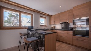 A modern kitchen with wooden cabinets, a marble island, bar stools, and large windows with a mountain view. - Chalet Brunner 2 (Lauterbrunnen)