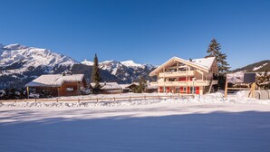 A hotel with a wooden facade, a red entrance, and a view of snow-covered mountains. - Chalet Brunner 2 (Lauterbrunnen)