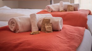 A hotel room with two beds, each with rolled towels and a red blanket. There is a wooden shelf above the beds and a window with a view of mountains. - Chalet Brunner 4 (Lauterbrunnen)