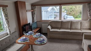 A cozy living room with a sofa, a dining table set for four, and a television. - Caravan Nearby Hastings, Coghurst Hall Park (Hastings)