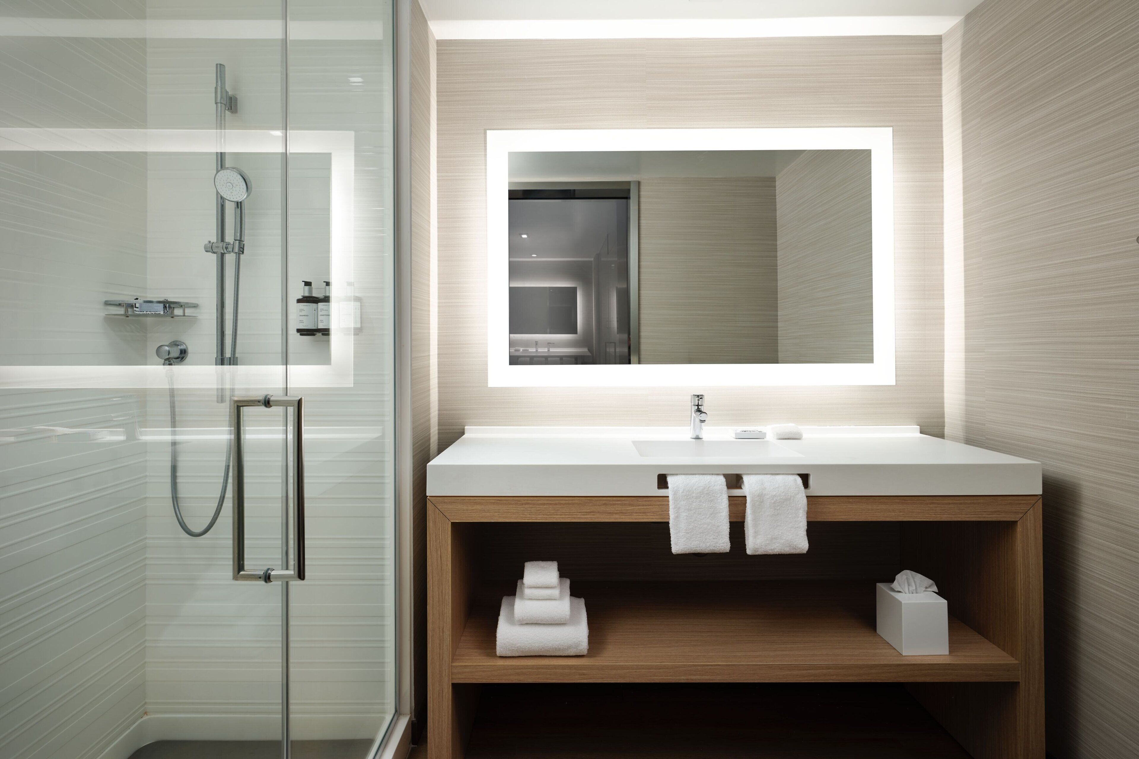 A modern bathroom with a glass shower enclosure, a wooden vanity with a large mirror, and built-in shelves.