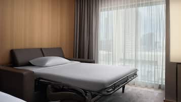 Ett modernt hotellrum med en säng, ett sängbord och ett fönster med tunna, genomskinliga gardiner.