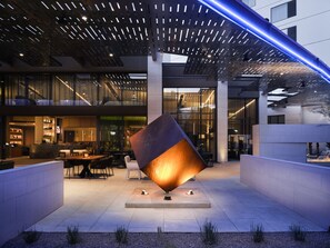 Un bâtiment moderne, avec une grande sculpture illuminée au centre, un espace bar doté de sièges et une vaste terrasse extérieure.