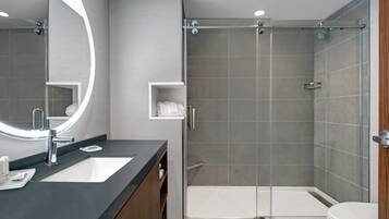 Un baño moderno con un espejo grande, un lavamanos, una ducha y un inodoro.
