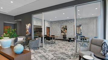 Un moderno vestíbulo de hotel con mostrador de recepción, zona de estar y una sala de conferencias visible a través de puertas de cristal.