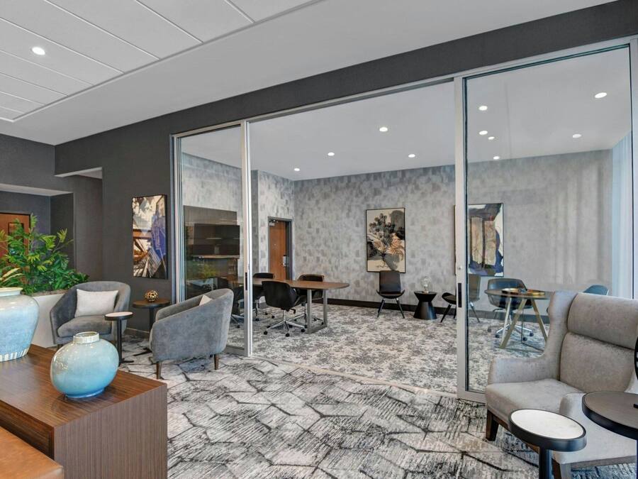 Eine moderne Hotelhalle mit Empfangstresen, einer Sitzecke und einem durch Glastüren einsehbaren Konferenzraum.