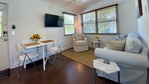 A living room with a white ceiling fan, a flat-screen TV mounted on the wall, a white sofa, a white armchair, and a small table with a vase of flowers. - 1/1 steps from downtown w/bikes. clean & comfortable (West Palm Beach)