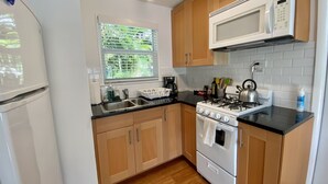 A kitchen with wooden cabinets, a white stove, a microwave, and a sink. - Studio steps from Intracoastal & downtown WPB with bikes (West Palm Beach)