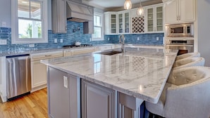 A modern kitchen with a marble island, stainless steel appliances, and pendant lighting. - Relaxing home, just a short walk to the beach and the Intracoastal Waterway (Wrightsville Beach)