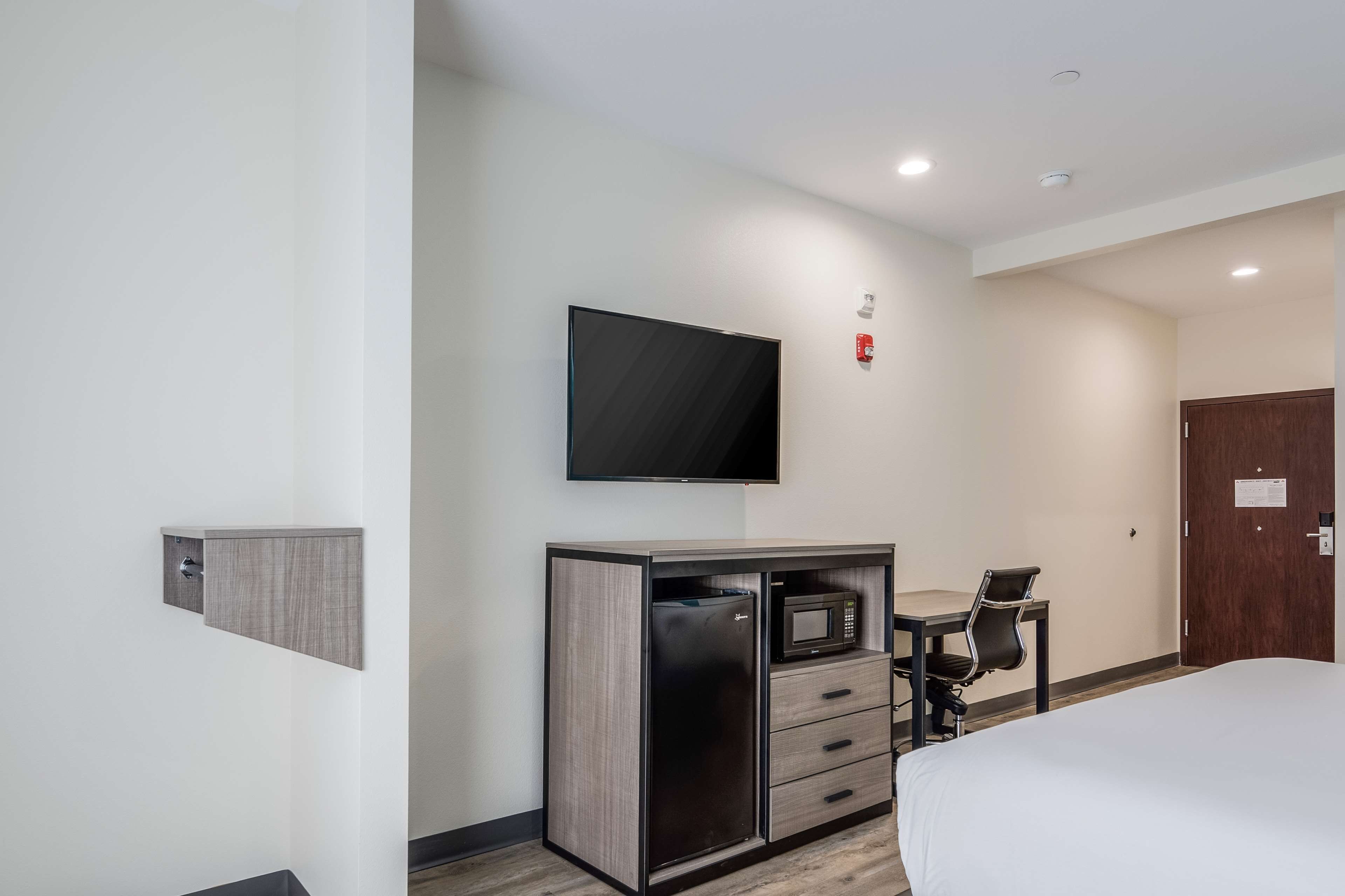A hotel room with a bed, a desk with a chair, a television, and a minibar.