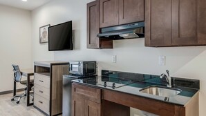 Une cuisine compacte équipée d’un four à micro-ondes, d’une cuisinière et d’un évier. On y trouve une chaise et un petit bureau avec des tiroirs.
