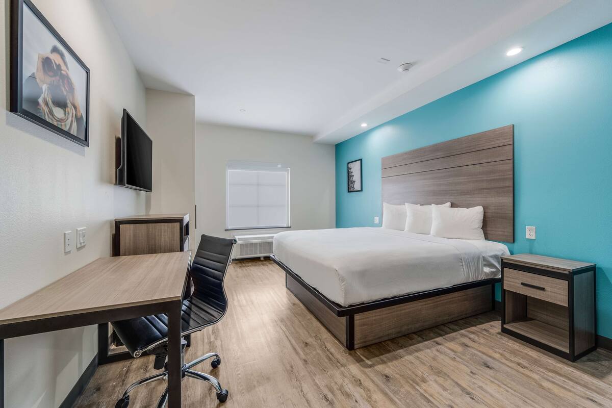 Una habitación de hotel moderna con cama, escritorio, silla y televisor instalado en la pared.
