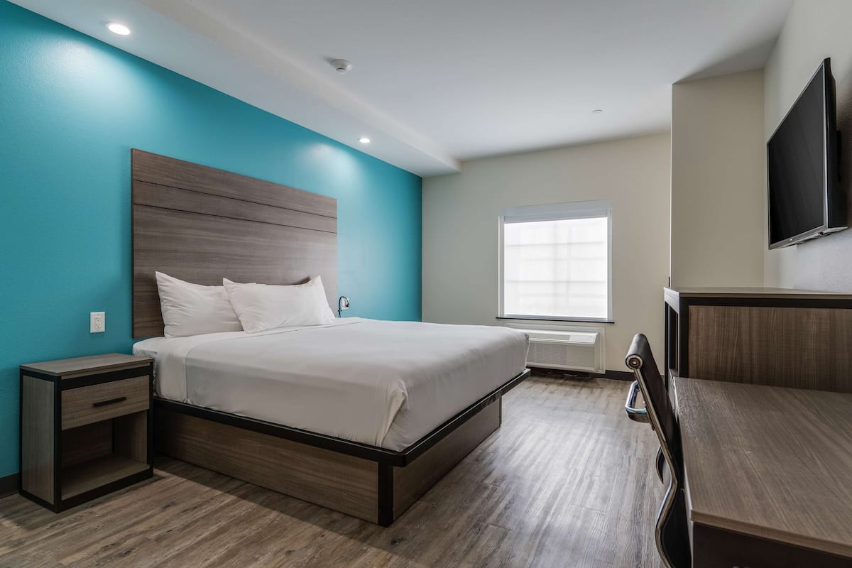 Habitación de hotel moderna con una cama grande, una mesita de noche, un escritorio y un televisor montado en la pared.