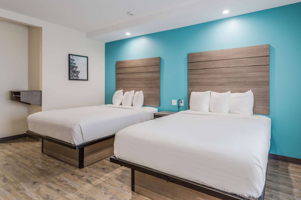 Habitación de hotel con dos camas, cabecera de madera, un cuadro enmarcado en la pared y suelo de madera.