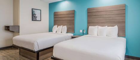 A hotel room with two beds, a wooden headboard, a framed picture on the wall, and a wooden floor.