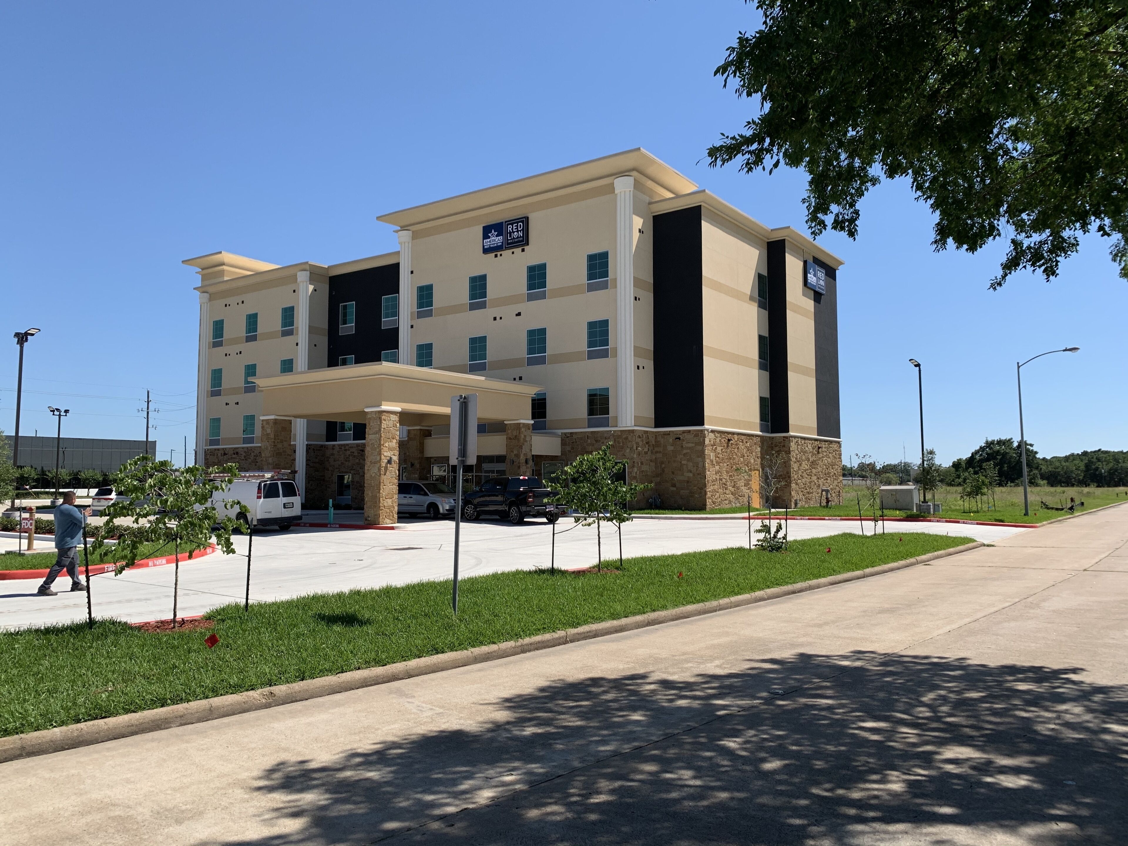 A multi-story hotel with a covered entrance, a parking lot, and a well-maintained lawn.