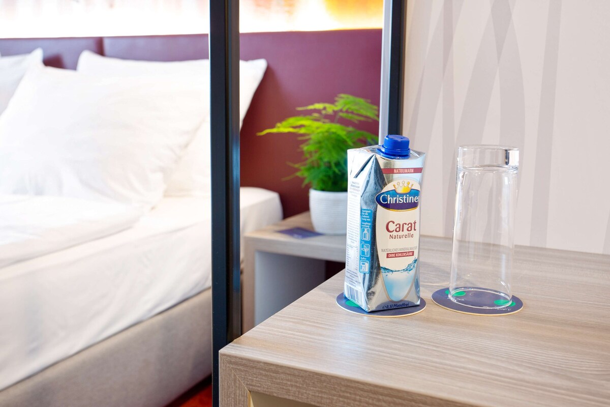 A carton of Carat Naturquelle orange juice and a glass on a wooden table in a hotel room.