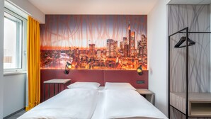 Una habitación de hotel con una cama, una mesita de noche, una lámpara de pared y un mural con un paisaje urbano.