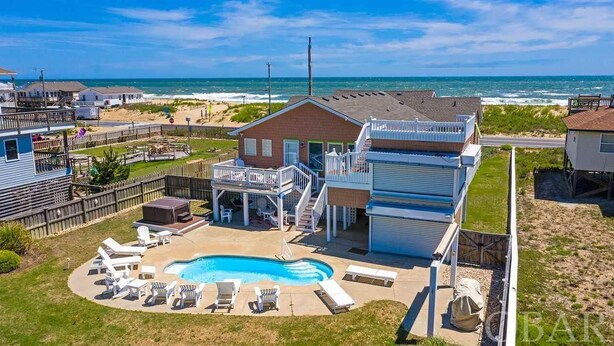 A beachfront property with a swimming pool, lounge chairs, and a deck overlooking the ocean. - Pet Friendly, Ocean Views, Pool & Hot Tub! (Kitty Hawk)