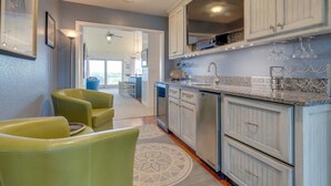 A kitchen with white cabinets, a granite countertop, and a backsplash with a beach theme. There are two green chairs and a patterned rug. - Pet Friendly, Ocean Views, Pool & Hot Tub! (Kitty Hawk)