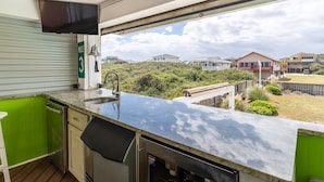 A kitchen with a sink, a microwave, and a refrigerator. There is a green wall and a window overlooking a residential area. - Pet Friendly, Ocean Views, Pool & Hot Tub! (Kitty Hawk)