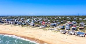 A coastal residential area with houses along the beach, a clear sky, and a lighthouse in the distance. - Pet Friendly, Ocean Views, Pool & Hot Tub! (Kitty Hawk)
