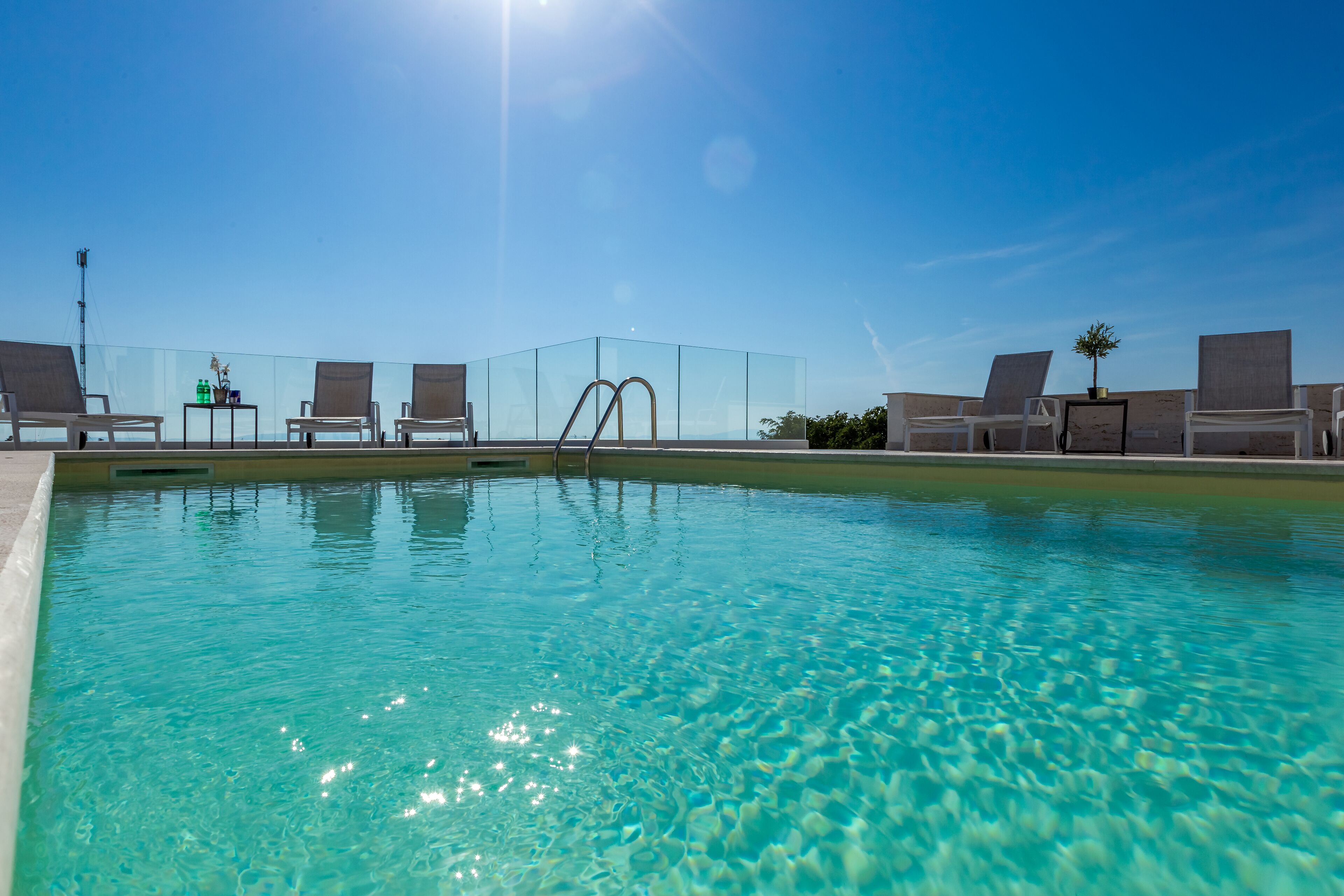 A clear blue pool with lounge chairs and a glass-enclosed area.