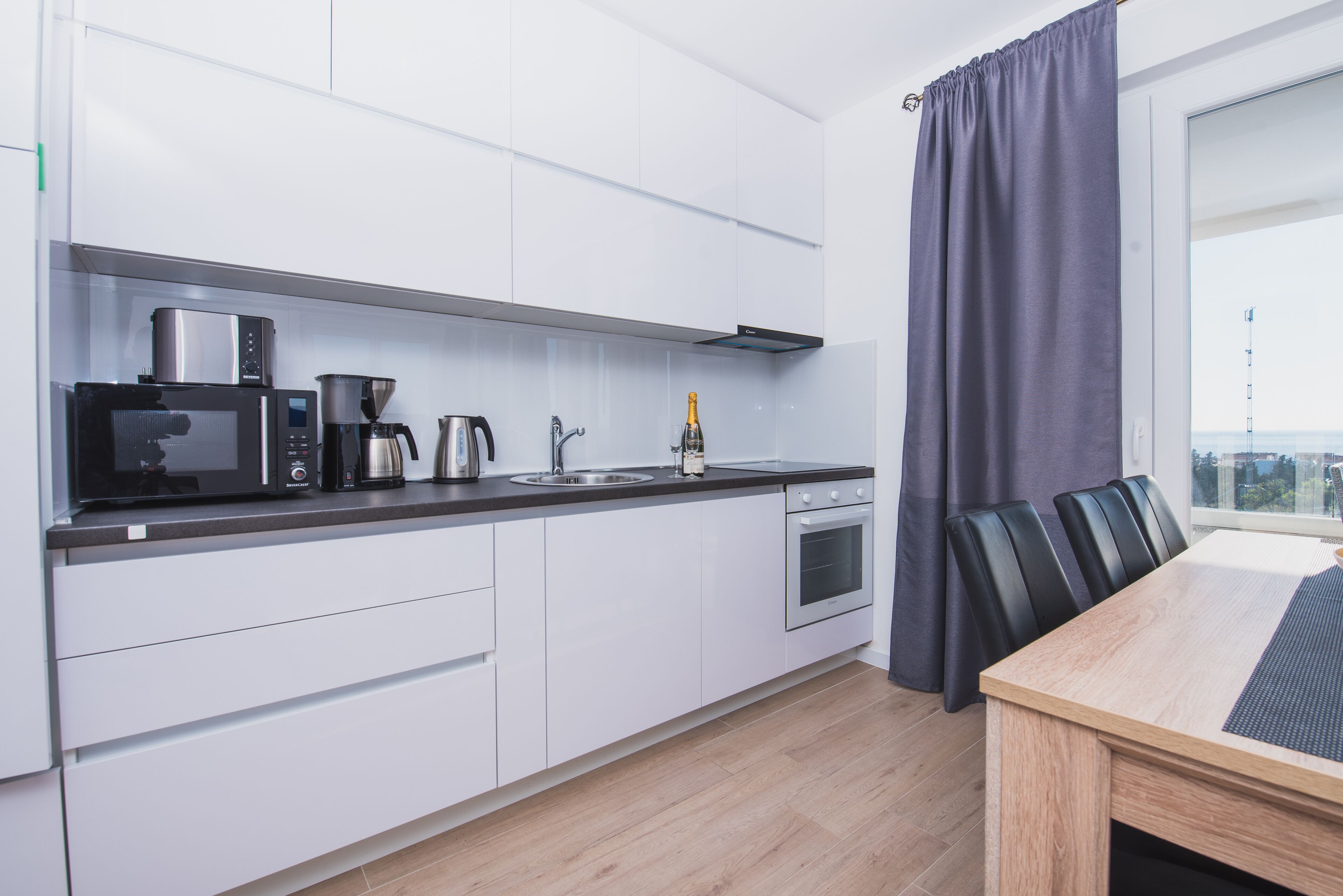 Een moderne keuken met witte kastjes, een magnetron, een koffiezetapparaat en een fles champagne.