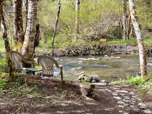 Un entorno tranquilo al aire libre con un arroyo cristalino, dos sillas de plástico y un sendero de piedra.
