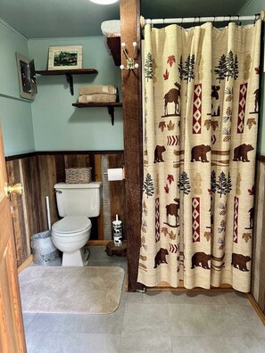 A bathroom with a toilet, a bidet, a shower curtain with animal prints, and a wooden shelf with a picture. - *Little Green Cabin on Big Creek * 5 mi to Mt. Rainier entrance! (Ashford)