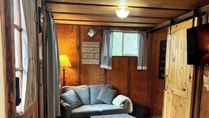 Acogedor interior de cabaña con techo de madera, un sofá, una mesa y dos taburetes.