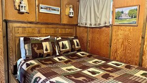 Un dormitorio con paneles de madera, edredón acolchado con estampados de animales, cabecera de madera, faroles sujetos a la pared y cuadros enmarcados.