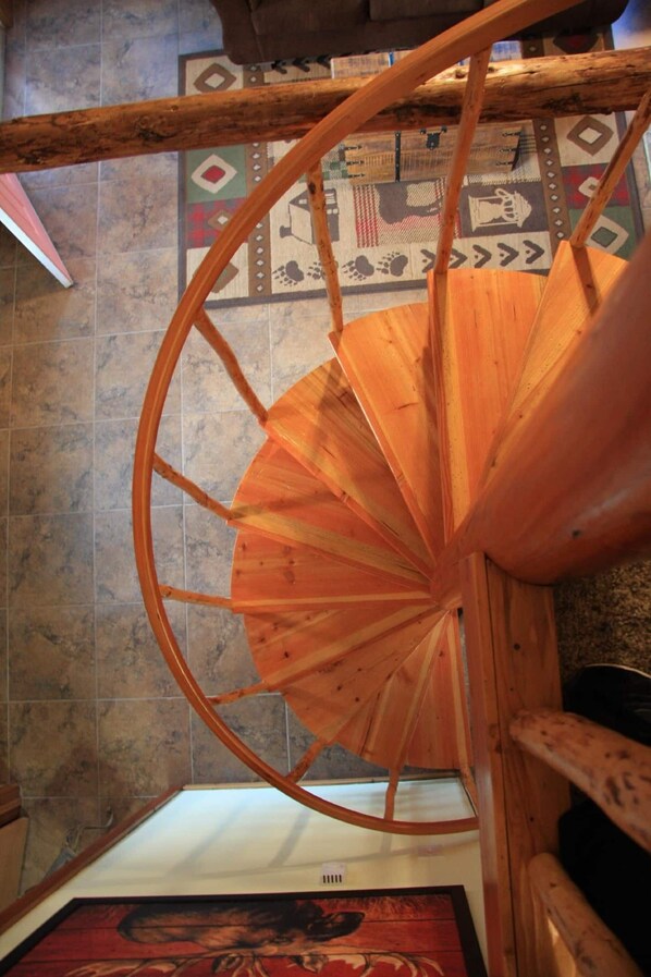 A wooden spiral staircase with a patterned floor below.