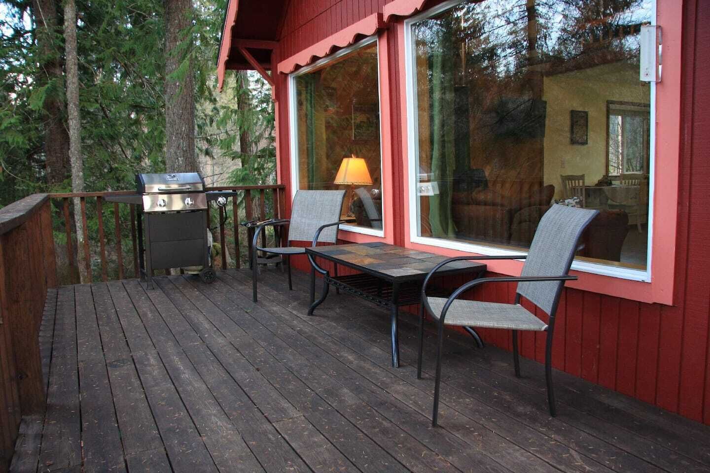 Een houten terras met een barbecue, twee stoelen en een tafel.