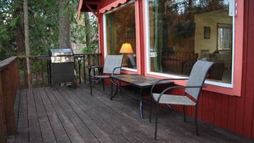 Een houten terras met een barbecue, twee stoelen en een tafel.