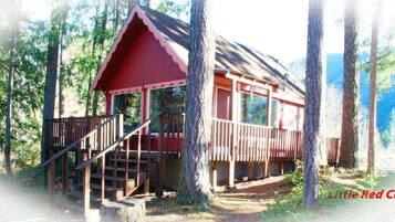 Een chalet met een rood dak, een houten terras en een trap naar een veranda.