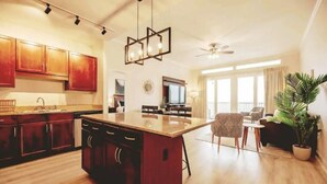 A spacious living area with a large wooden dining table, a kitchen with dark wooden cabinets, a central island, and a ceiling fan.