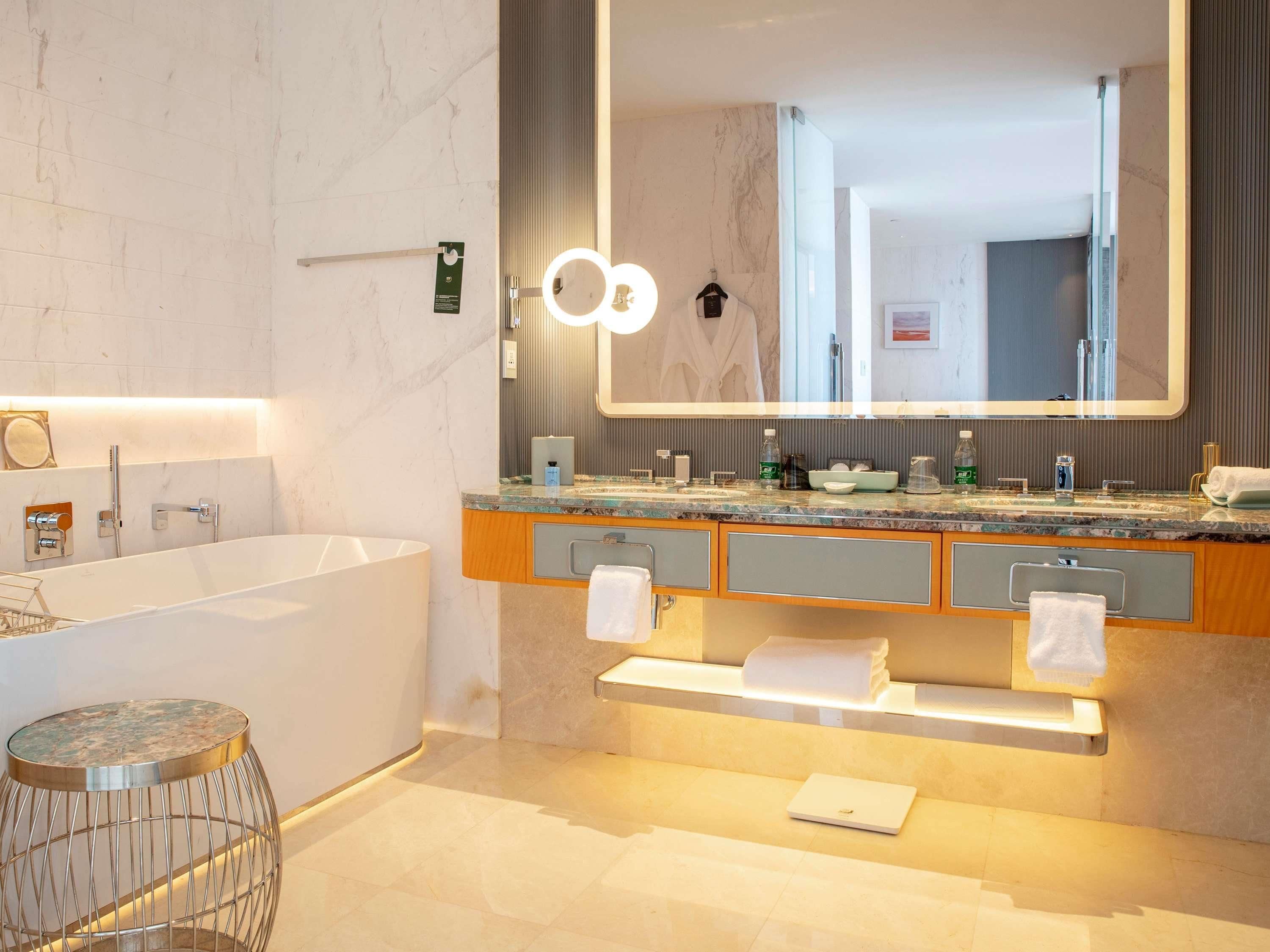 A modern bathroom with a large mirror, a bathtub, and a vanity with a countertop.
