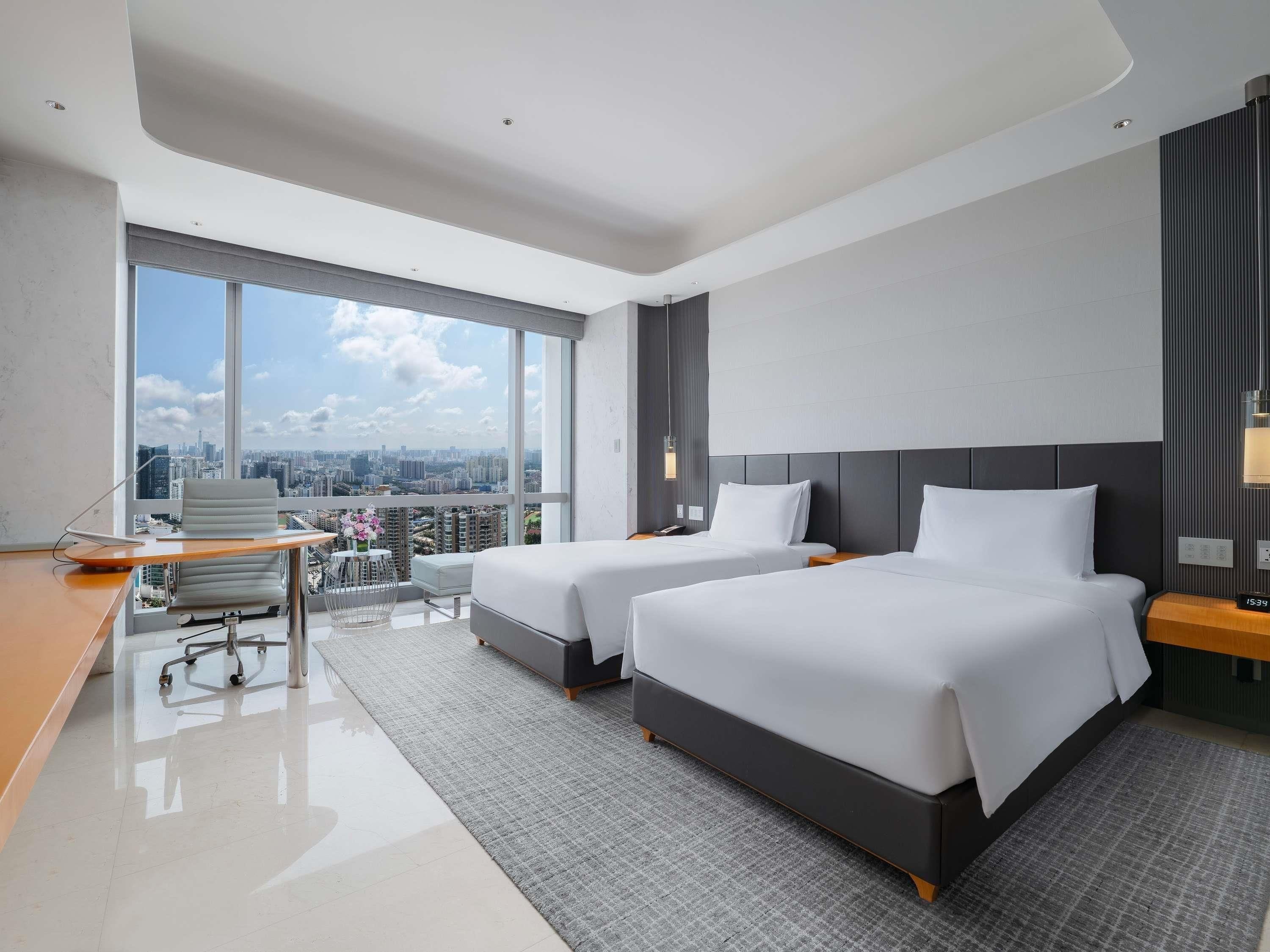 Une chambre d’hôtel moderne avec deux lits, un bureau et une grande fenêtre donnant sur la ville.