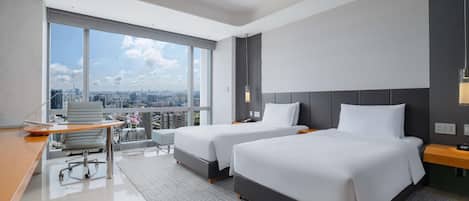 Una habitación de hotel moderna con dos camas, un escritorio y un amplio ventanal con vistas a la ciudad.