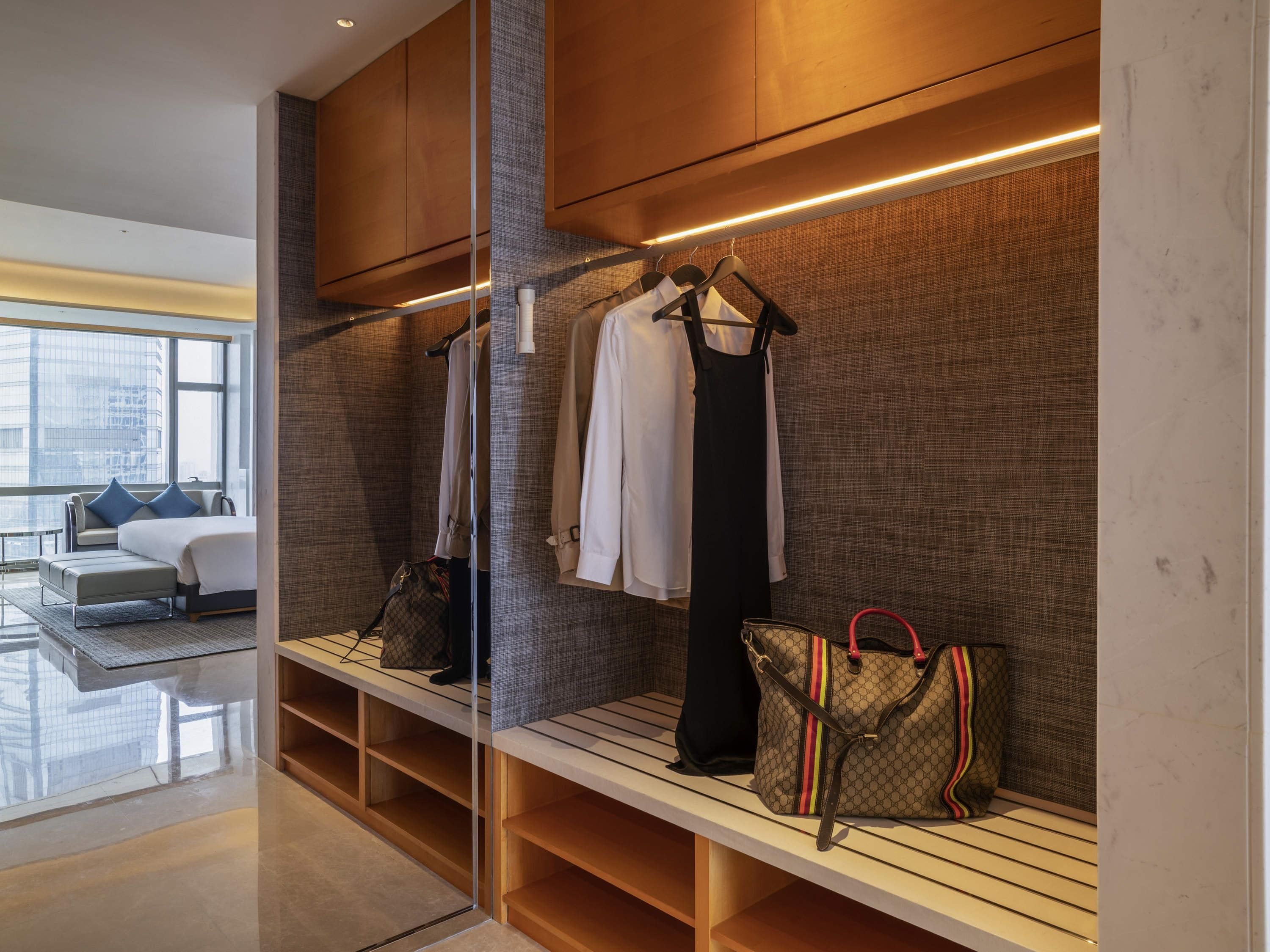 A modern hotel room with a built-in closet, a seating area with a sofa, and a view of the cityscape.