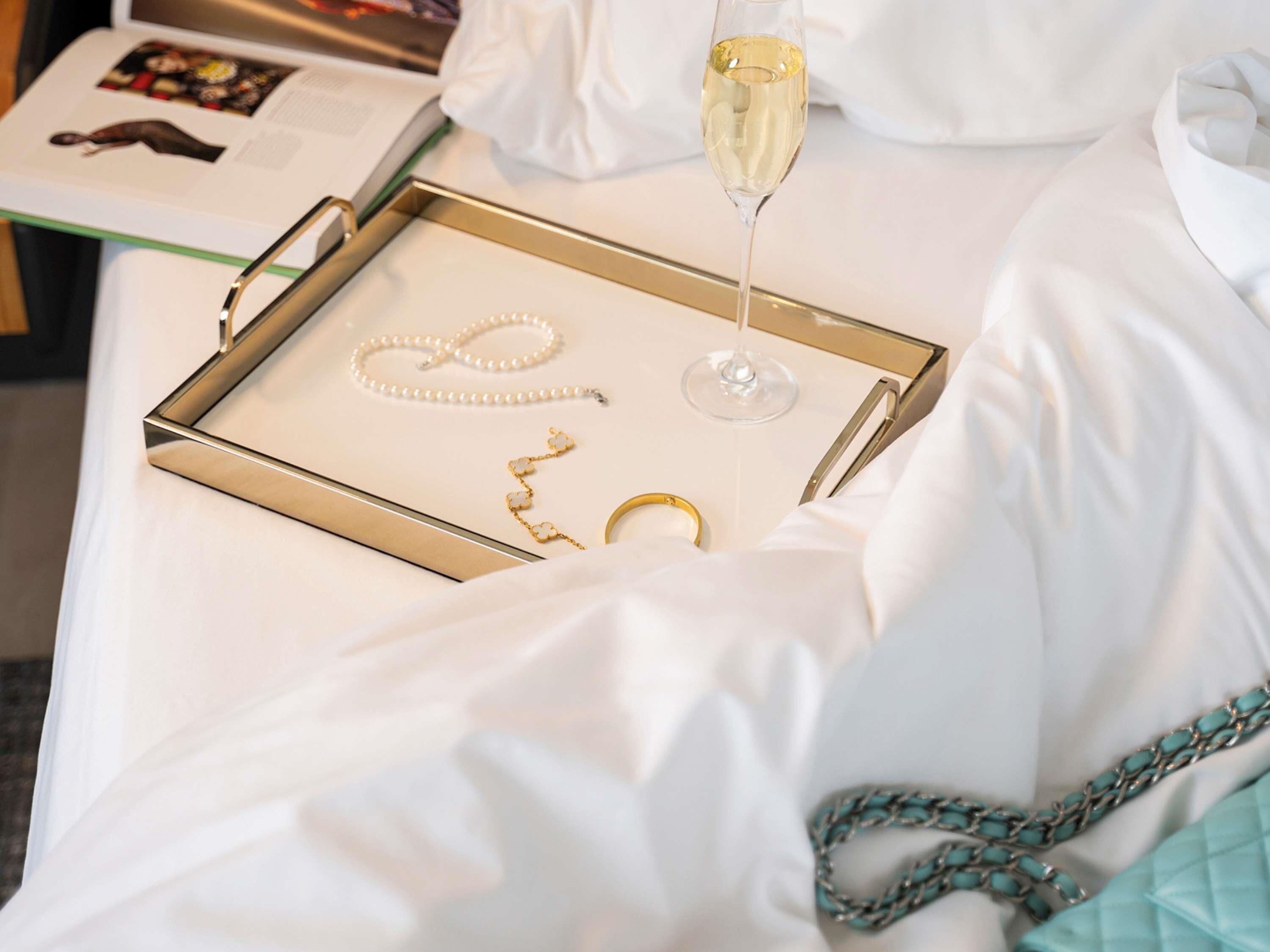 A bed with a tray containing jewelry, a glass of champagne, and a book.