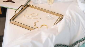 A bed with a tray containing jewelry, a glass of champagne, and a book.