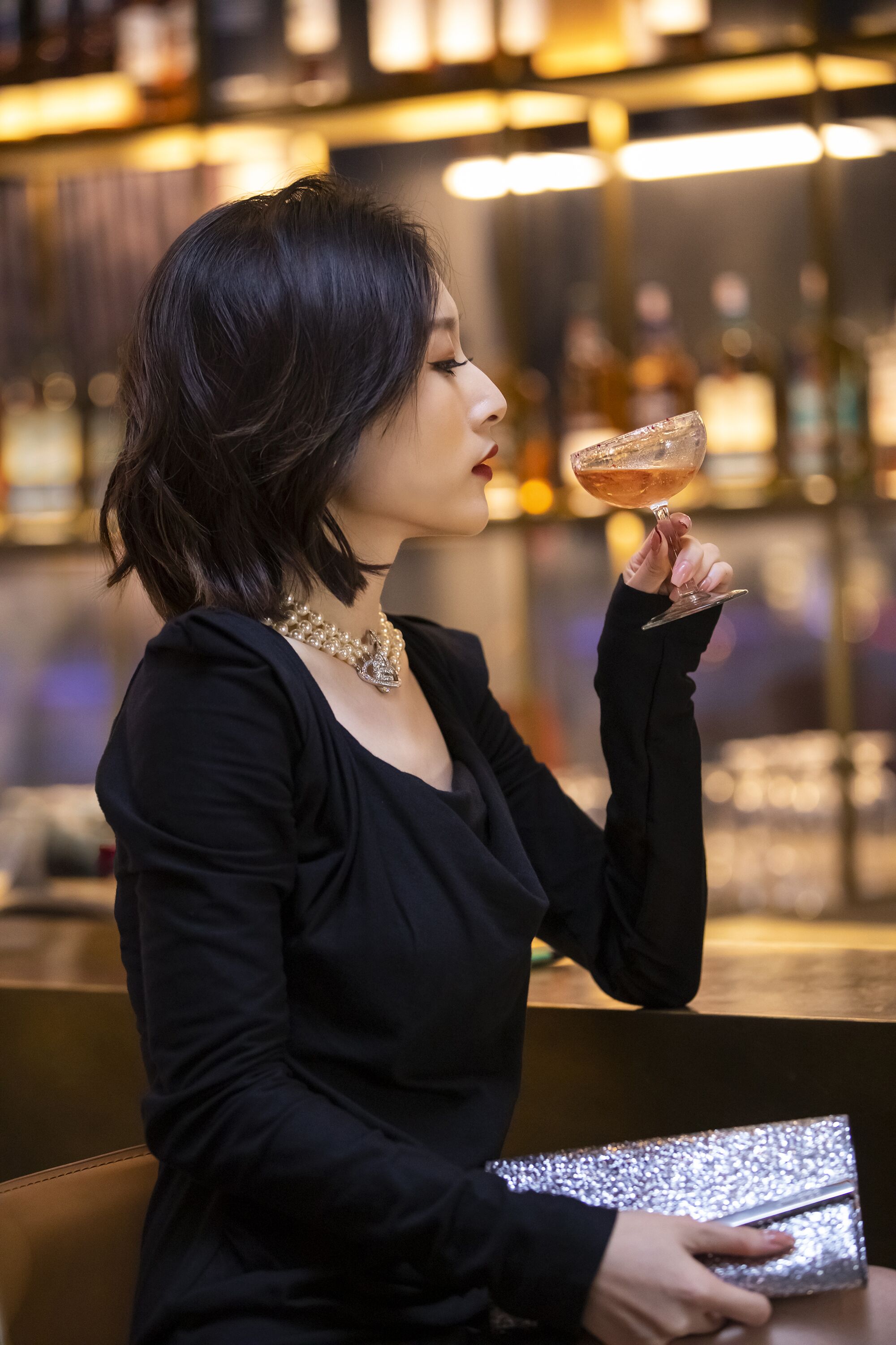 A person holding a drink in a bar setting with shelves of bottles in the background.