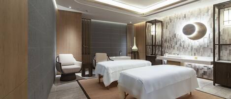 A modern hotel room with two beds, a sitting area, a large mirror, and a bathroom with a bathtub and sink.