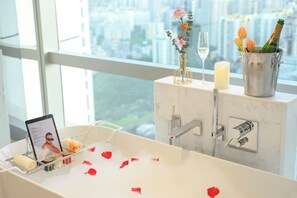 A bathroom with a bathtub, a vanity, a window with a city view, a candle, and a bottle of champagne. - Sofitel Haikou (Haikou)