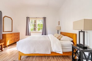 Une chambre à coucher avec un lit en bois, une commode, une table de chevet avec une lampe et une fenêtre avec des rideaux.