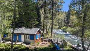 A cabin with a river view, outdoor seating, and a large rock nearby.